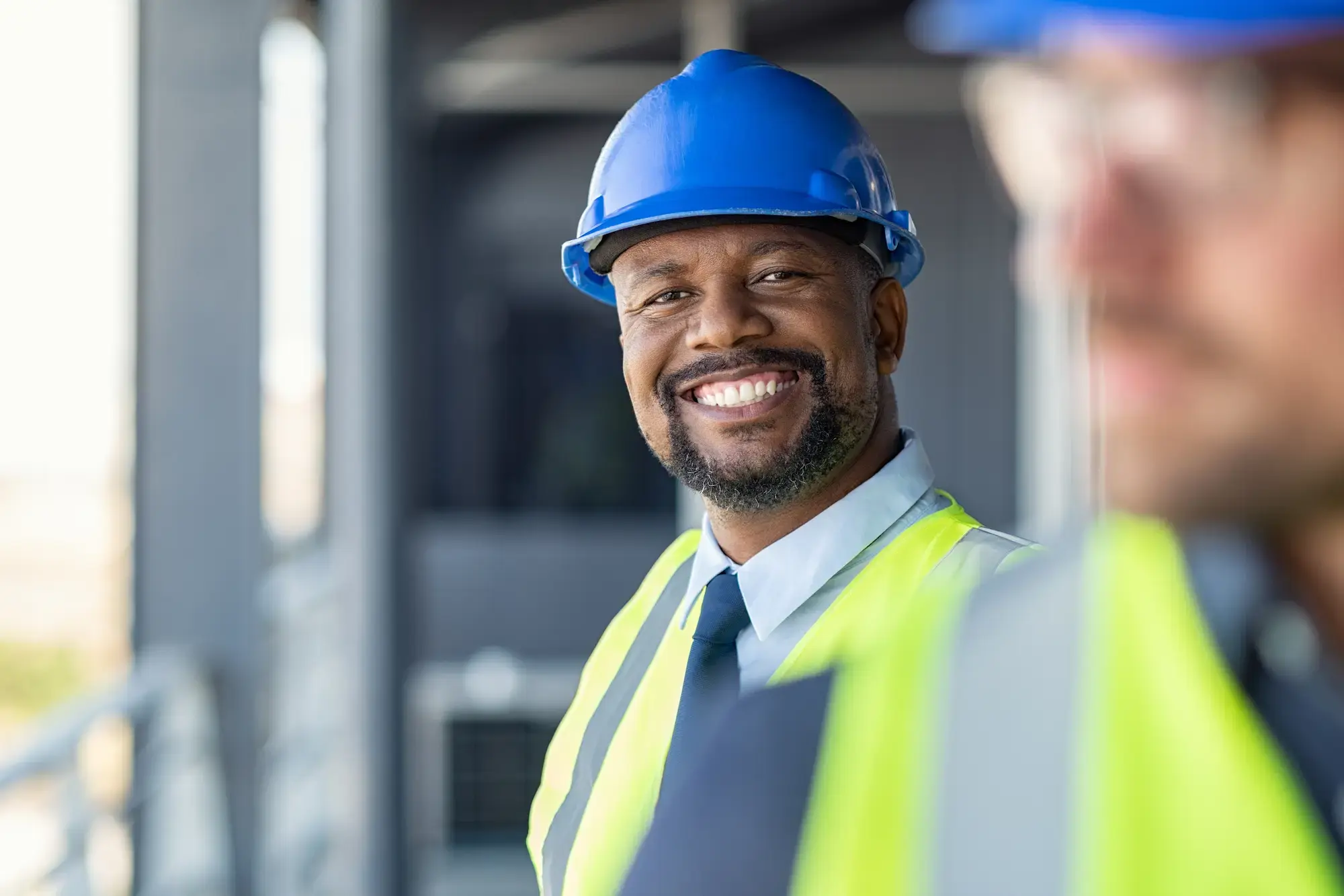 Two men in hard hats and vests stand side by side, representing teamwork in the roofing industry.