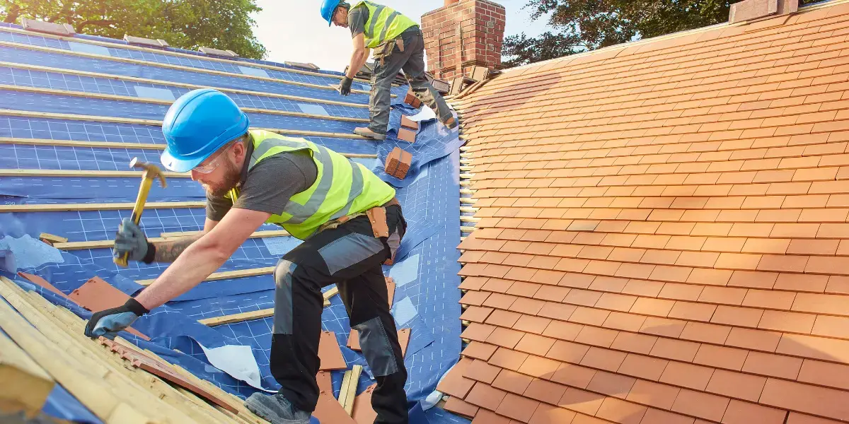 Two men using hammers to work on a roof, focusing on essential roofing codes and safety measures.