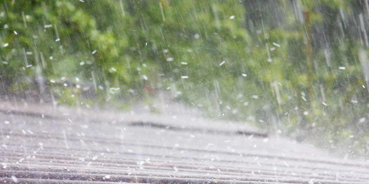 Rain cascades on a roof, framed by trees in the background, depicting a scene relevant to understanding hail damage claims.